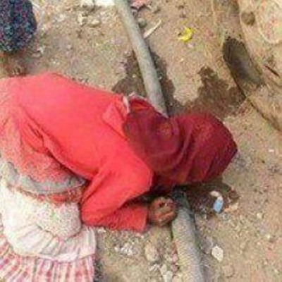 صورة لفتاة يمنية تعاني العطش وتشرب من أحد ثقوب ماسورة مياه
