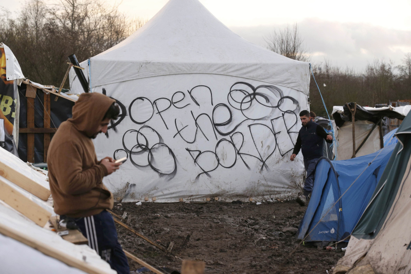 Migrants stand in the mud near a tent with the message, "Open the Border" that is located in a field called the Grande Synthe jungle, a camp of makeshift shelters where migrants and asylum seekers from Irak, Kurdistan and Syria gather in Grande-Synthe, France, December 29, 2015.  REUTERS/Pascal Rossignol