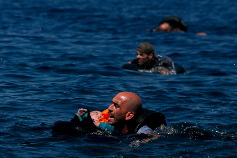 A Syrian refugee holding a baby in a lifetube swims towards the shore after their dinghy deflated some 100m away before reaching the Greek island of Lesbos, September 12, 2015.    REUTERS/Alkis Konstantinidis    SEARCH "YEAREND 2015: MIGRANT CRISIS" FOR ALL 55 PICTURES          TPX IMAGES OF THE DAY