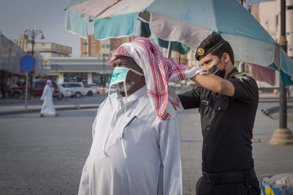 رجل أمن يساعد مواطنًا مسنًّا في ربط كمامته الطبية