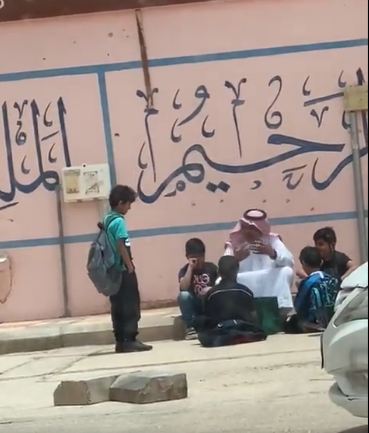 شاهد.. معلم ينتظر مع طلابه على الرصيف لحين وصول ذويهم