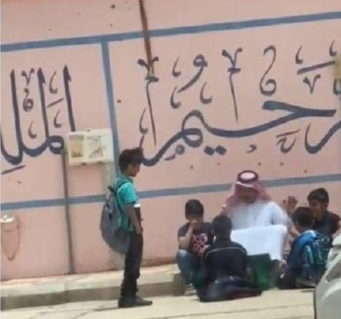 معلم يجلس مع طلابه أمام المدرسة بعد تأخر أولياء أمورهم
