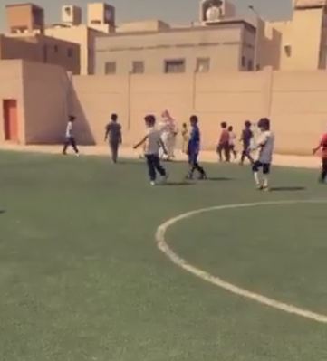 معلم يساعد طالباً مقعداً بمشاركة زملائه في لعبة كرة القدم